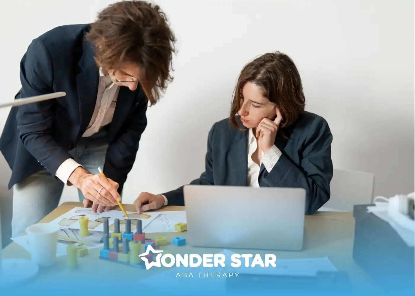 Two autistic adults reviewing printed charts & models at a desk, representing workplace planning & cognitive problem solving.
