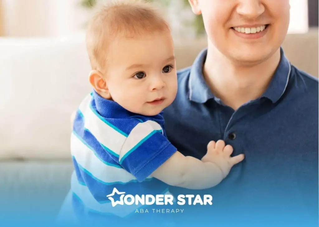 Autistic baby boy in striped shirt being held by smiling therapist indoors, looking curiously off to the side.