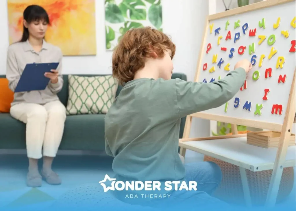 Autistic young boy placing magnetic alphabet letters on board while therapist observes and takes notes in background.