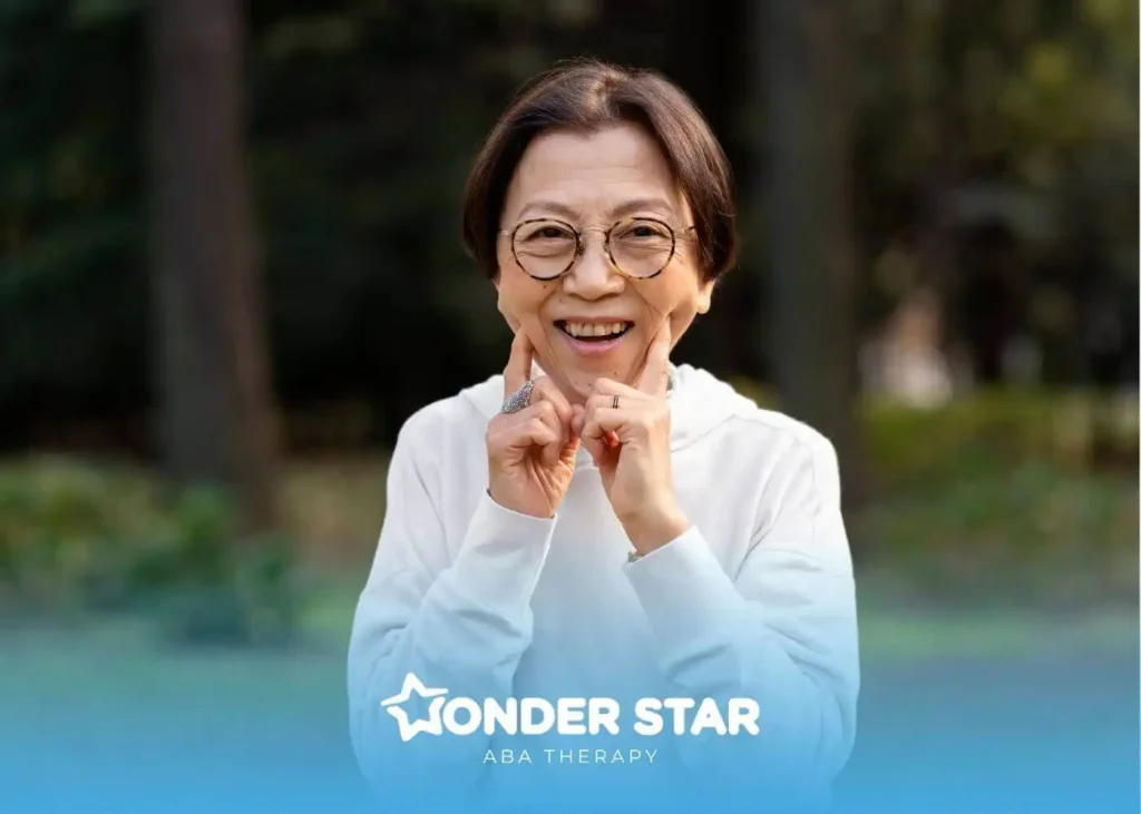 Autistic senior woman wearing glasses outdoors, gently touching her cheeks with both hands in a sunny park setting.
