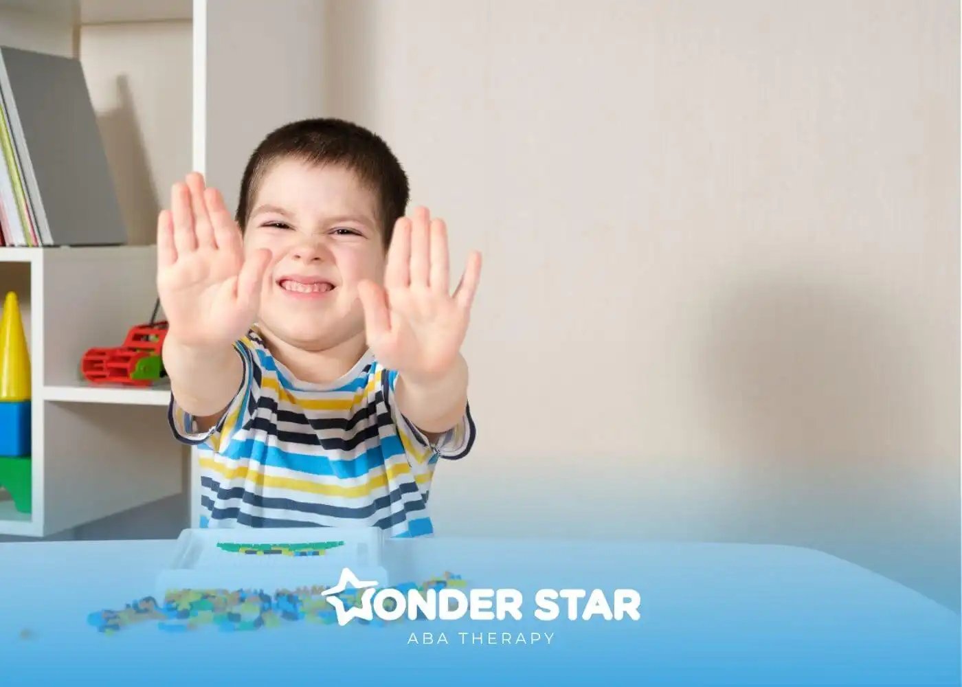 Smiling autistic child raising both hands during tabletop activity with small colorful beads and fine motor toys.