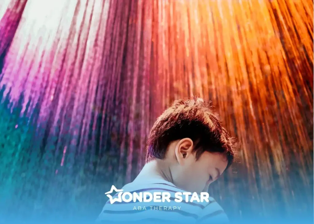 Autistic child standing under colorful sensory light installation, looking down while vibrant rainbow lights shine above.