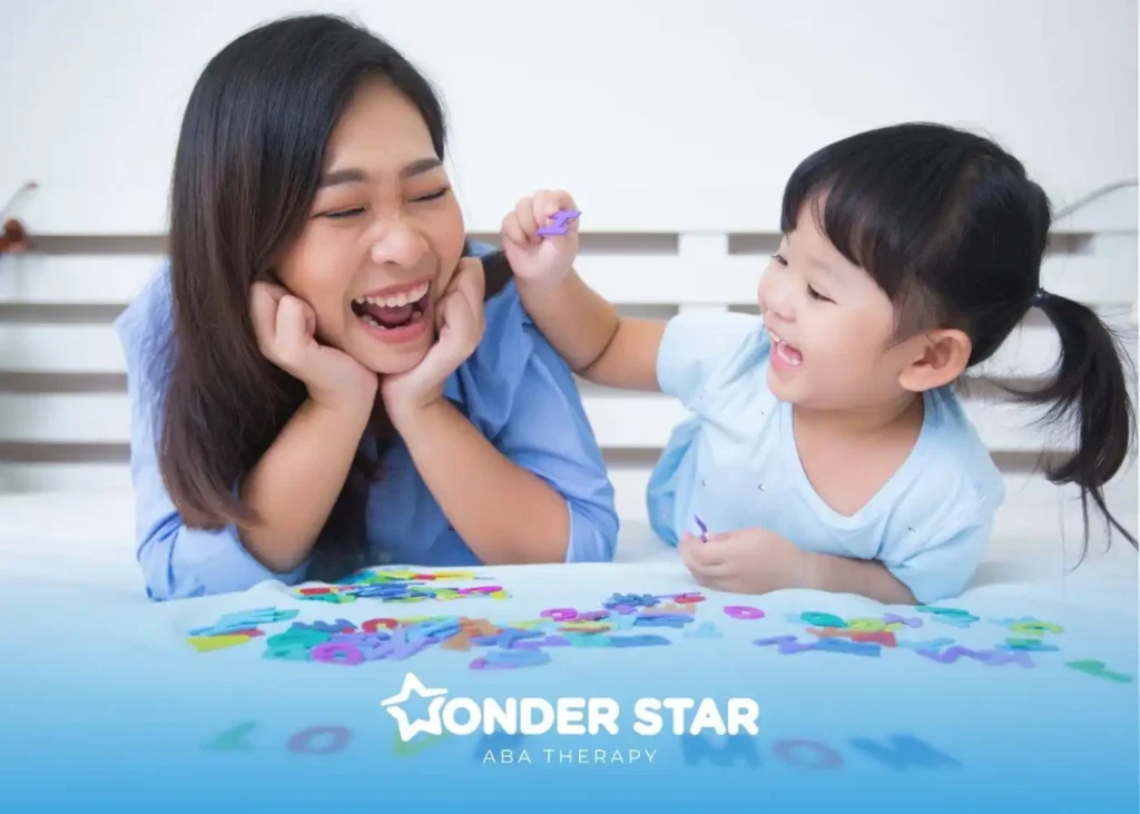 A therapist and autistic baby laughing together while playing with colorful alphabet letters on a white table.