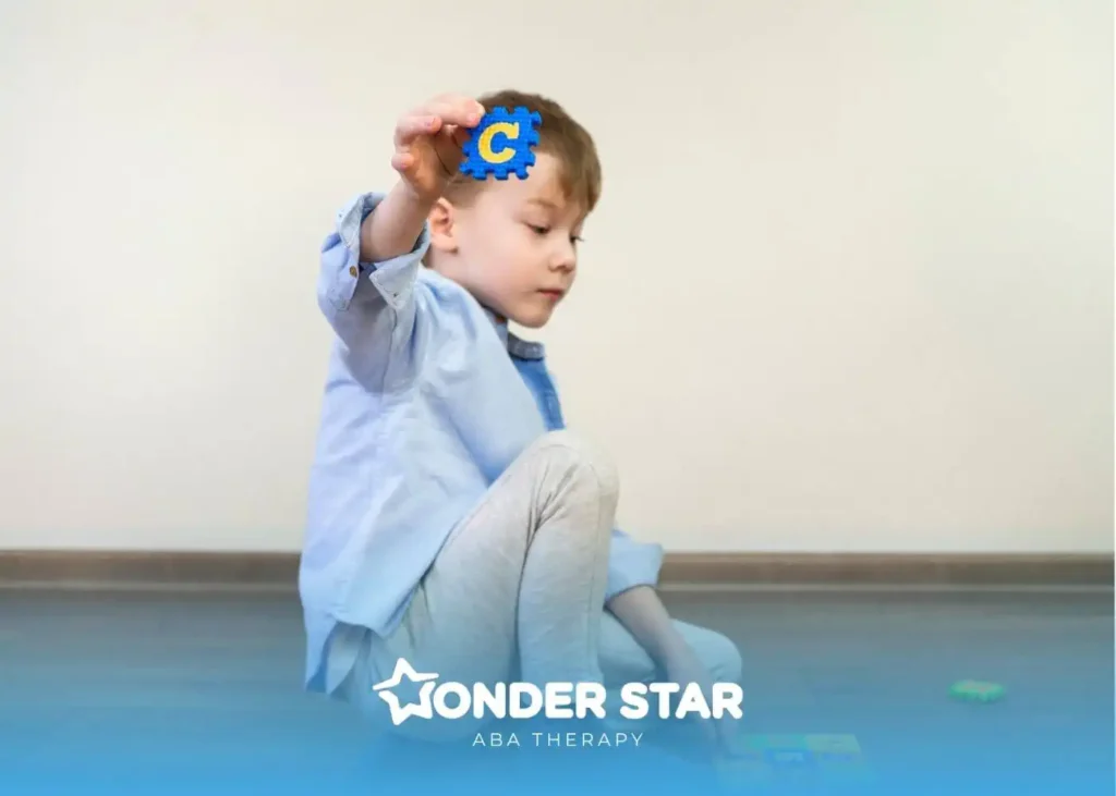 Autistic boy sitting on the floor holding a foam alphabet letter “C,” practicing early literacy and letter recognition skills