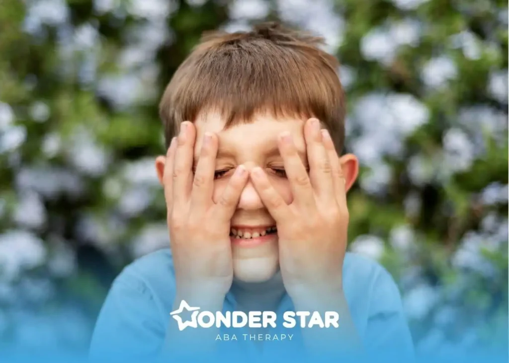 Autistic child smiles while covering eyes, illustrating social communication differences like reduced eye contact.