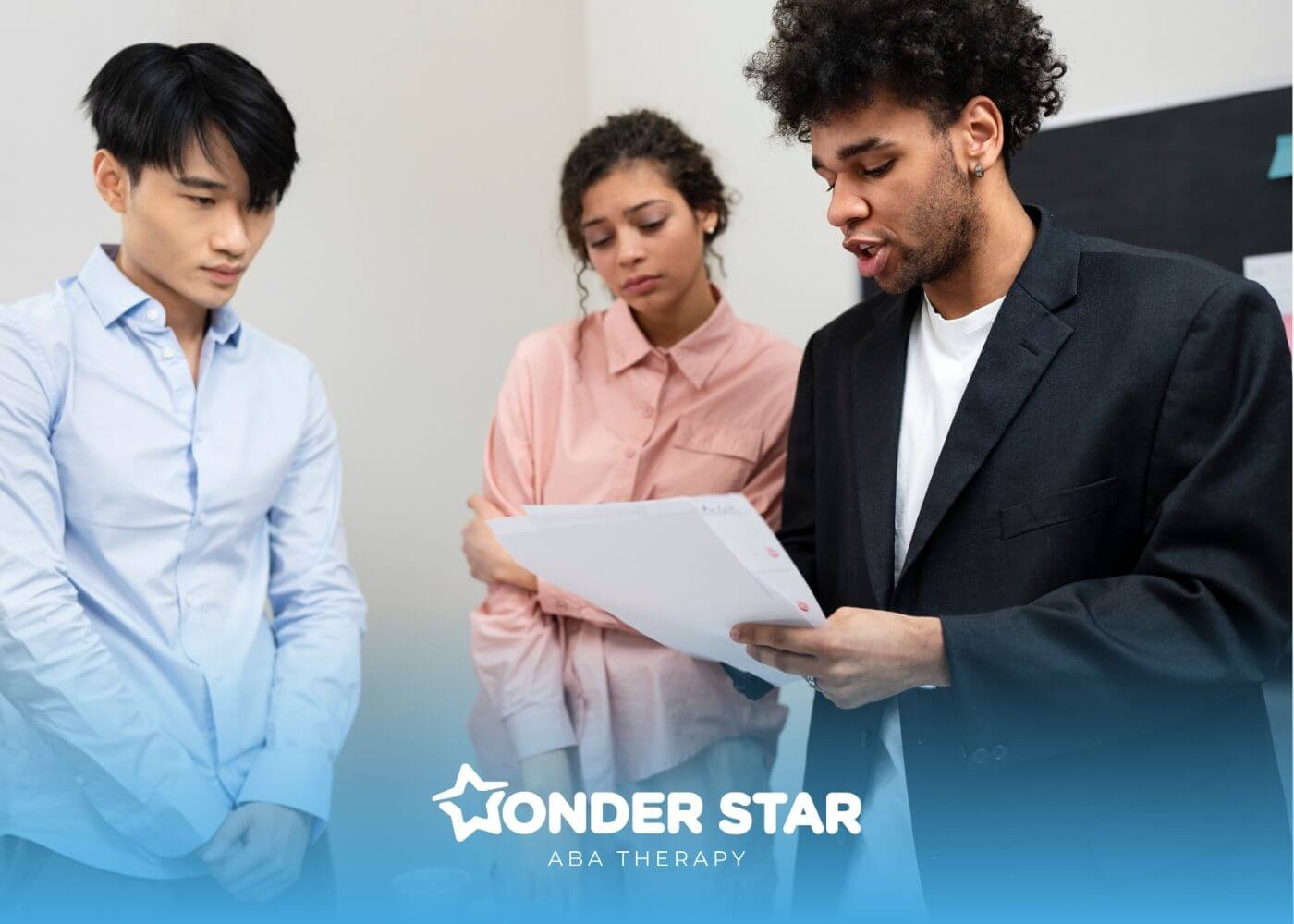 Three therapists standing together reviewing documents as one person explains information during a workplace discussion.