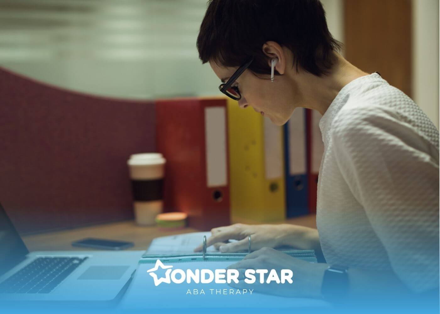 ABA woman studying at a desk with a laptop and binder while reviewing notes and documents during a focused study session.