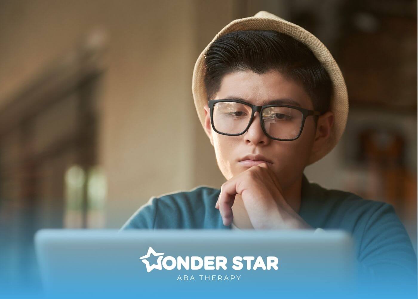 Young male ABA wearing glasses and a hat concentrating on a laptop screen while studying or working online.